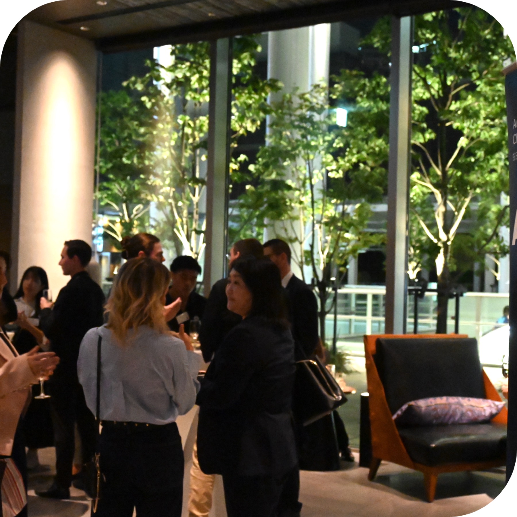 Members talking over drinks at an ANZCCJ reception beside a glass wall